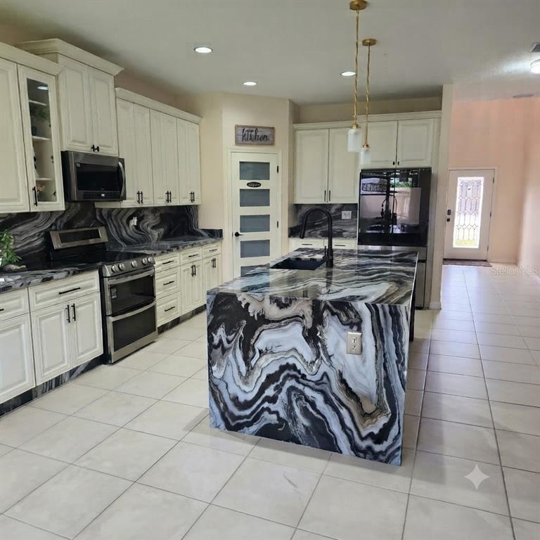 A kitchen features white cabinetry, stainless steel appliances, and a bold black-and-white marble waterfall island — 7559 SWEETER TIDE TRAIL, WESLEY CHAPEL, FL