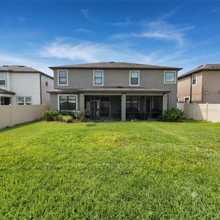 The rear exterior of a two-story house features a screened-in patio and a fenced yard — 7559 SWEETER TIDE TRAIL, WESLEY CHAPEL, FL