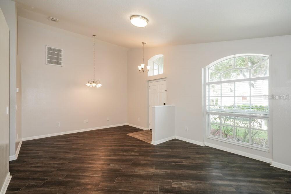 An empty dining room features dark wood-look flooring, vaulted ceilings, and a large arched window — 6410 BUCKHEAD COURT, WESLEY CHAPEL, FL