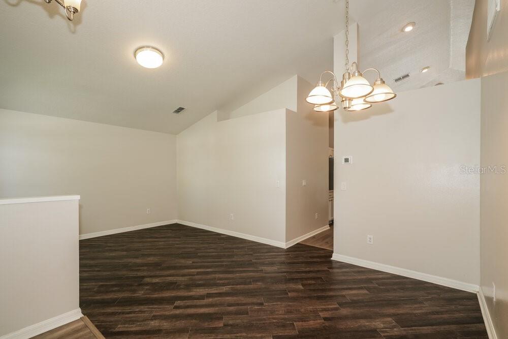 An interior view of a room with dark wood-look flooring, light walls, and a chandelier — 6410 BUCKHEAD COURT, WESLEY CHAPEL, FL