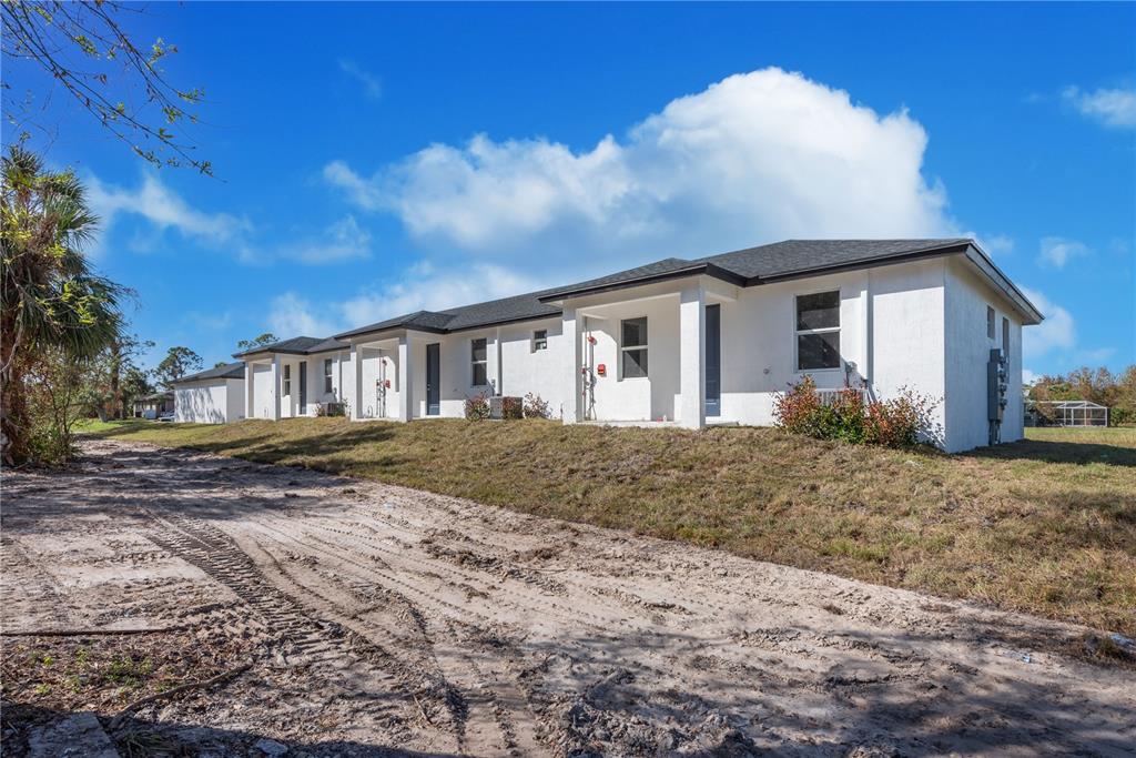 A row of white, single-story residential units with dark roofs sits along a dirt path — 260 ROTONDA BOULEVARD, ROTONDA WEST, FL