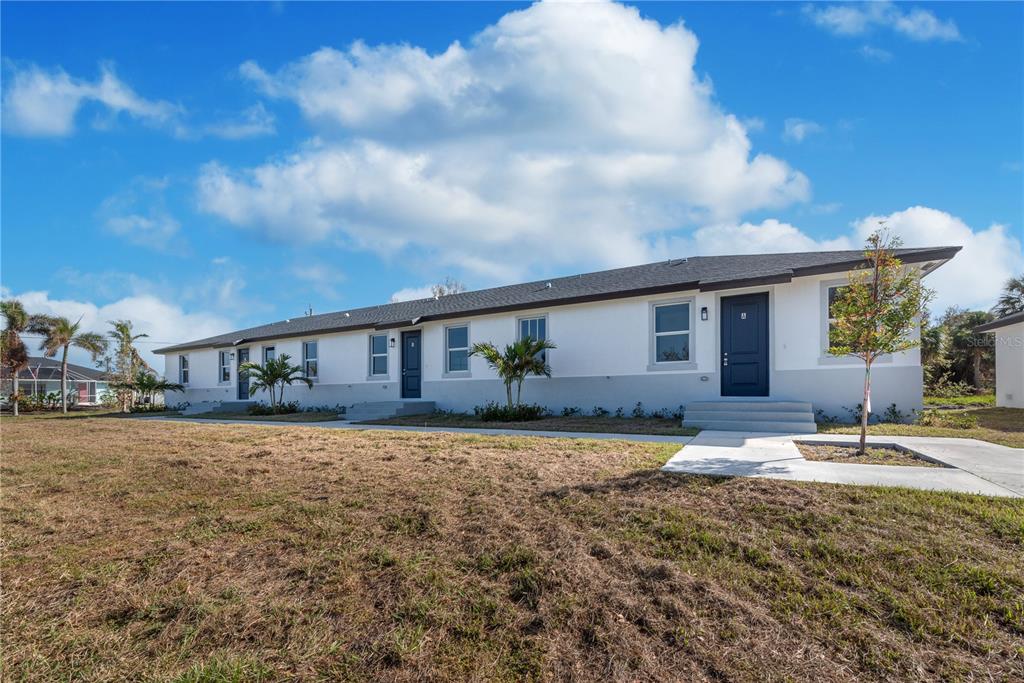 A single-story duplex with white walls, dark doors, and a gray roof under a blue sky — 260 ROTONDA BOULEVARD, ROTONDA WEST, FL
