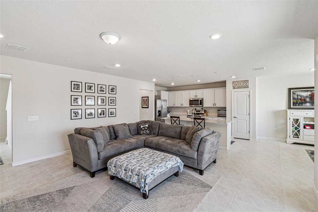 A living room with a gray sectional sofa, ottoman, and an open kitchen in the background — 2210 LOVELY LANE, DAVENPORT, FL
