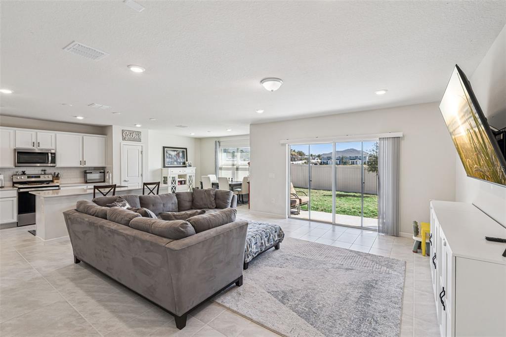 An open-concept living room with a gray sectional sofa, tile floors, and sliding glass doors — 2210 LOVELY LANE, DAVENPORT, FL