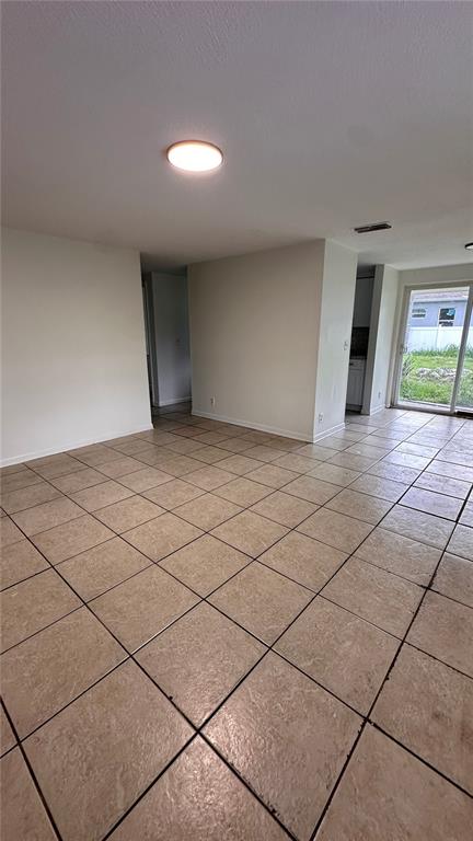 An empty room with beige tile flooring, white walls, a ceiling light, and sliding glass doors — 3311 E CHELSEA STREET, TAMPA, FL