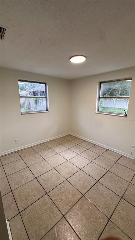 An empty room features beige tiled flooring, white walls, two windows, and a ceiling light — 3311 E CHELSEA STREET, TAMPA, FL