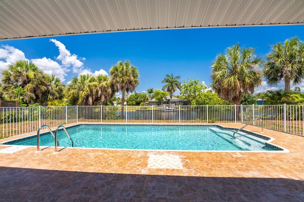 A rectangular swimming pool sits on a tiled patio behind a white metal fence — 18321 WOLBRETTE CIRCLE, PORT CHARLOTTE, FL