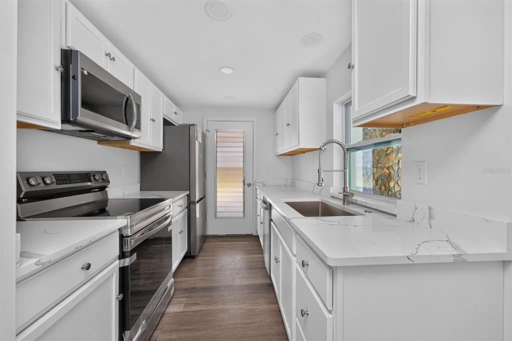 A galley kitchen features white cabinets, marble-look countertops, stainless steel appliances, and wood-look flooring — 18321 WOLBRETTE CIRCLE, PORT CHARLOTTE, FL