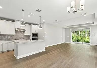 A modern kitchen features white cabinetry, a central island, and light wood flooring — 15 MULBERRY ROAD, PALM COAST, FL