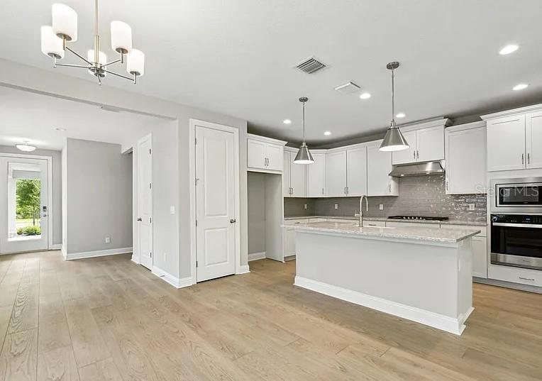 A modern kitchen features white cabinetry, a central island, and light wood flooring — 15 MULBERRY ROAD, PALM COAST, FL
