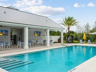 A swimming pool sits in front of a covered outdoor patio with seating and televisions — 15 MULBERRY ROAD, PALM COAST, FL