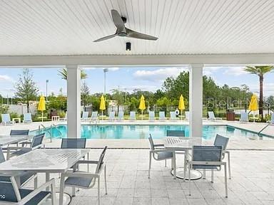 A covered patio with a ceiling fan overlooks a swimming pool with yellow umbrellas — 15 MULBERRY ROAD, PALM COAST, FL