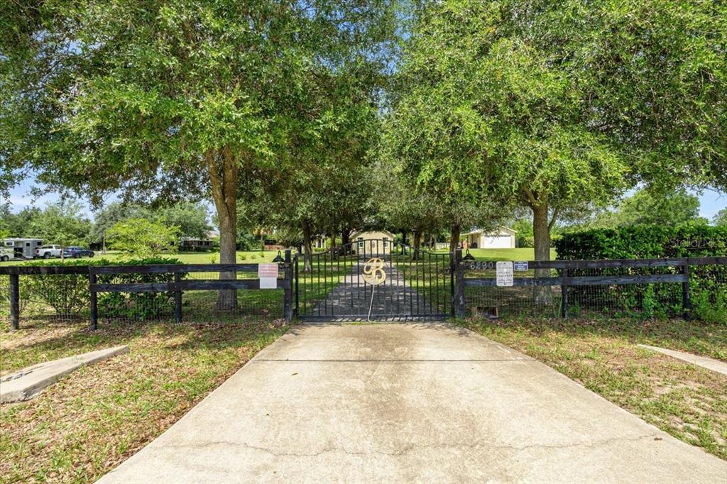 A concrete driveway leads to a gated entrance with a large letter B ornament — 6290 SE 178TH COURT, MORRISTON, FL