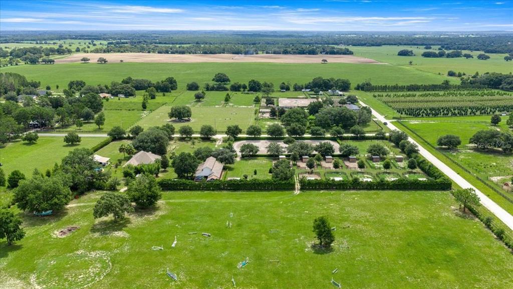 An aerial view of a rural property featuring a house, stables, and fenced pastures — 6290 SE 178TH COURT, MORRISTON, FL