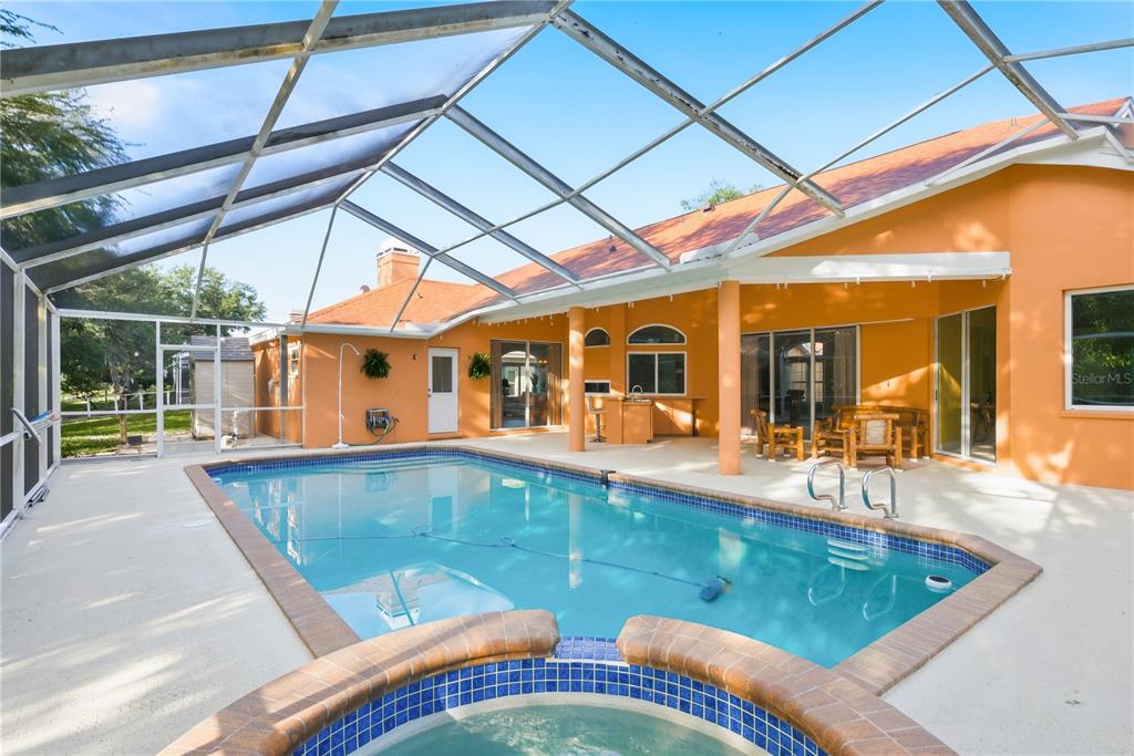 A swimming pool and hot tub are enclosed within a screened lanai behind a house — 791 WEATHERSFIELD DRIVE, DUNEDIN, FL
