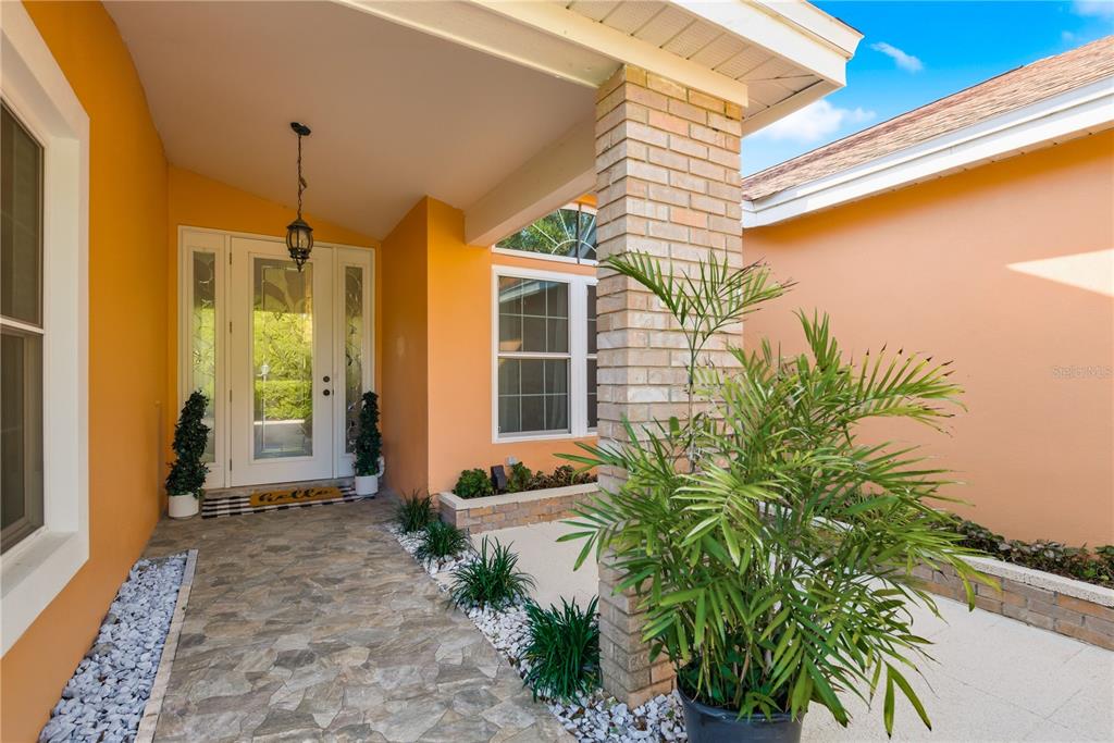 A covered entryway features a stone walkway, orange walls, a brick pillar, and a front door — 791 WEATHERSFIELD DRIVE, DUNEDIN, FL