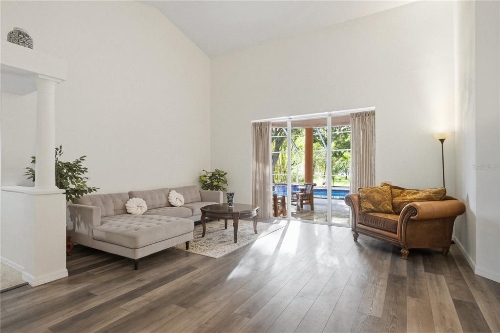 A living room with vaulted ceilings, wood-look flooring, a sectional sofa, and sliding glass doors — 791 WEATHERSFIELD DRIVE, DUNEDIN, FL