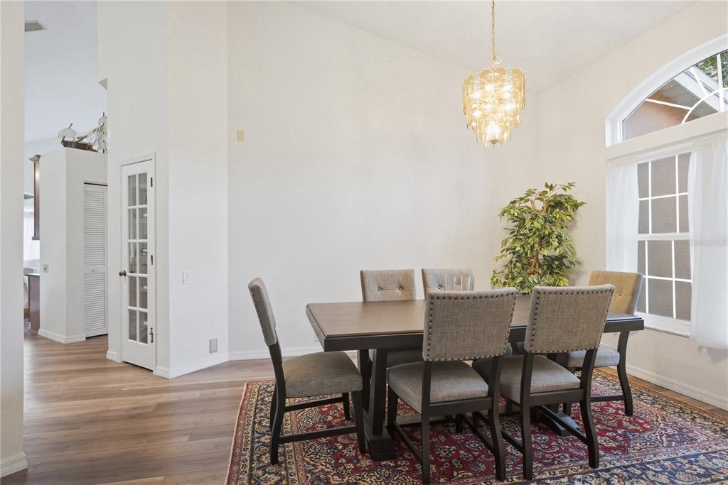 A dining room features a wooden table, six upholstered chairs, a chandelier, and an area rug — 791 WEATHERSFIELD DRIVE, DUNEDIN, FL