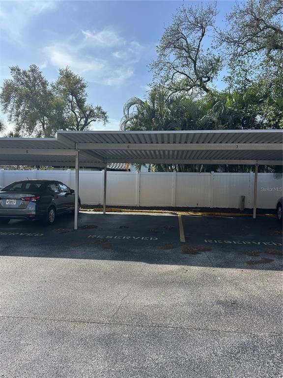 A covered parking area features numbered spaces and a white privacy fence in the background — 11485 OAKHURST ROAD UNIT 200-307, LARGO, FL