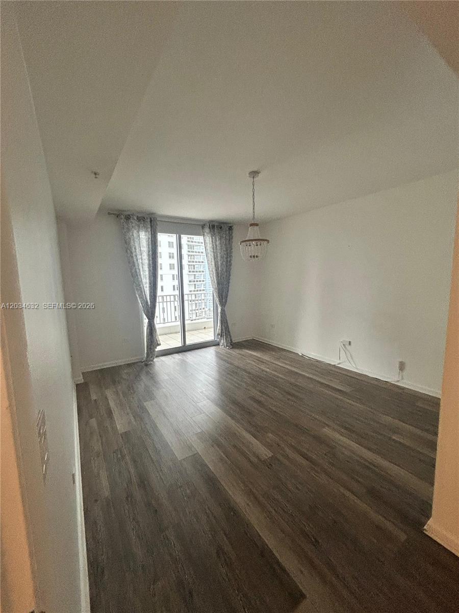An empty room features wood-look flooring, a beaded chandelier, and a sliding glass balcony door — 801 Brickell Key Blvd # 1710, Miami FL 33131, MIAMI, FL
