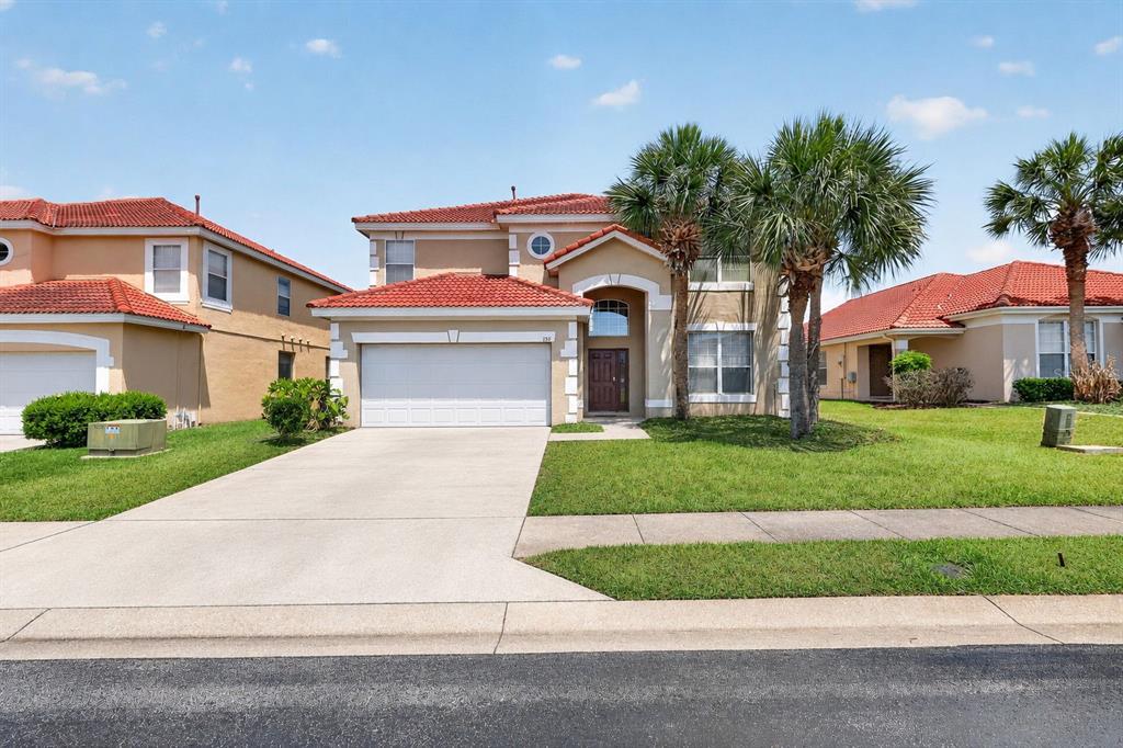 A two-story suburban house with a red tile roof, beige stucco, and a concrete driveway — 130 SARAGOSSA AVENUE, DAVENPORT, FL