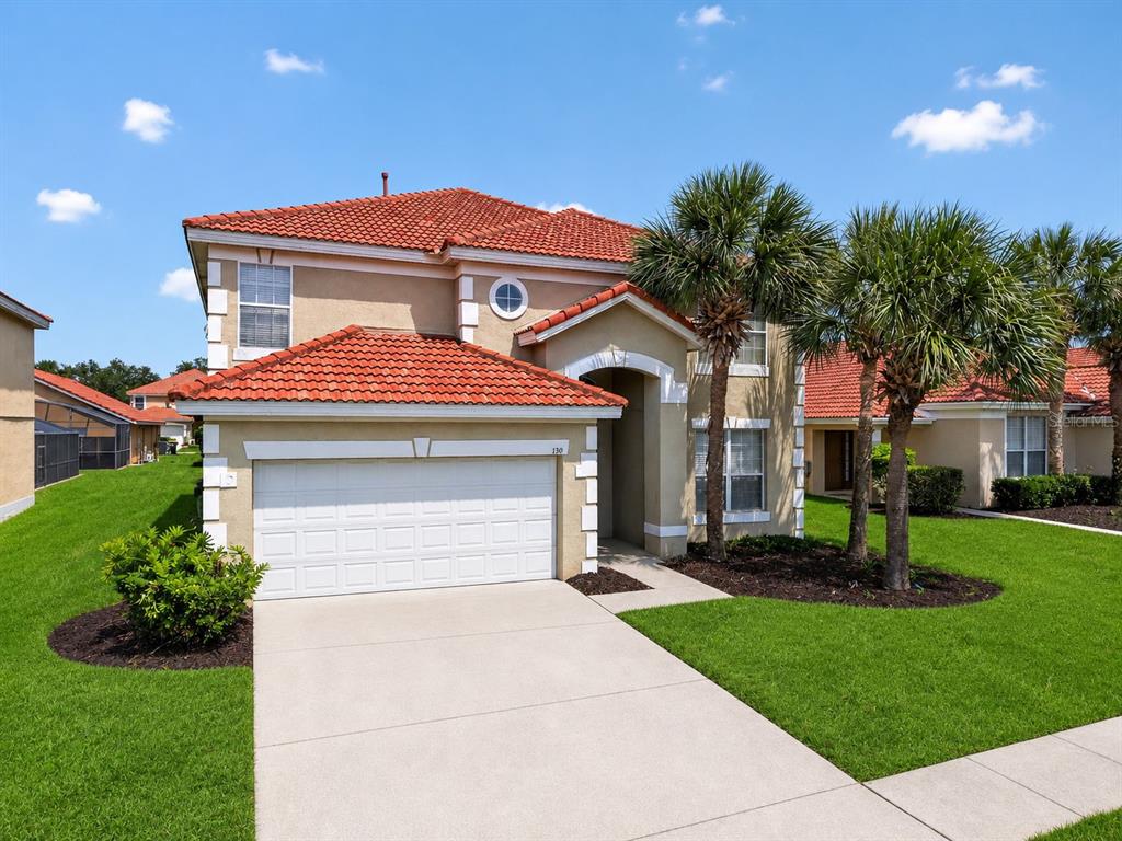 A two-story house with a red tile roof, beige stucco exterior, and a two-car garage — 130 SARAGOSSA AVENUE, DAVENPORT, FL