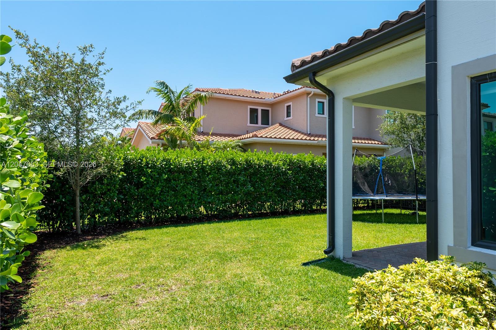 A grassy backyard features a hedge, a trampoline, and a covered patio area — 3412 Emerson Ln, Hollywood FL 33312, HOLLYWOOD, FL