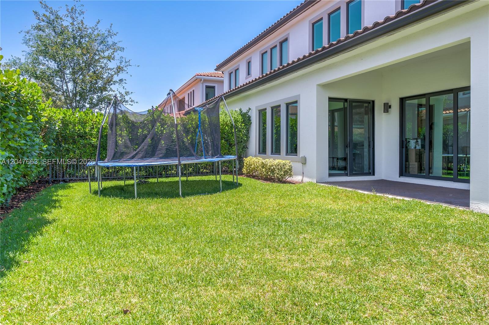 A backyard features a trampoline on a lawn next to a white house with sliding doors — 3412 Emerson Ln, Hollywood FL 33312, HOLLYWOOD, FL