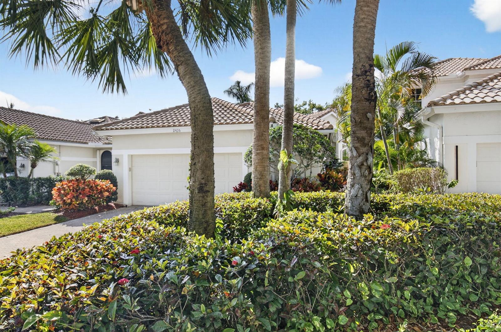 A view of a house exterior with a two-car garage, palm trees, and landscaping — 2476 NW 66th Drive, Boca Raton FL 33496, BOCA RATON, FL