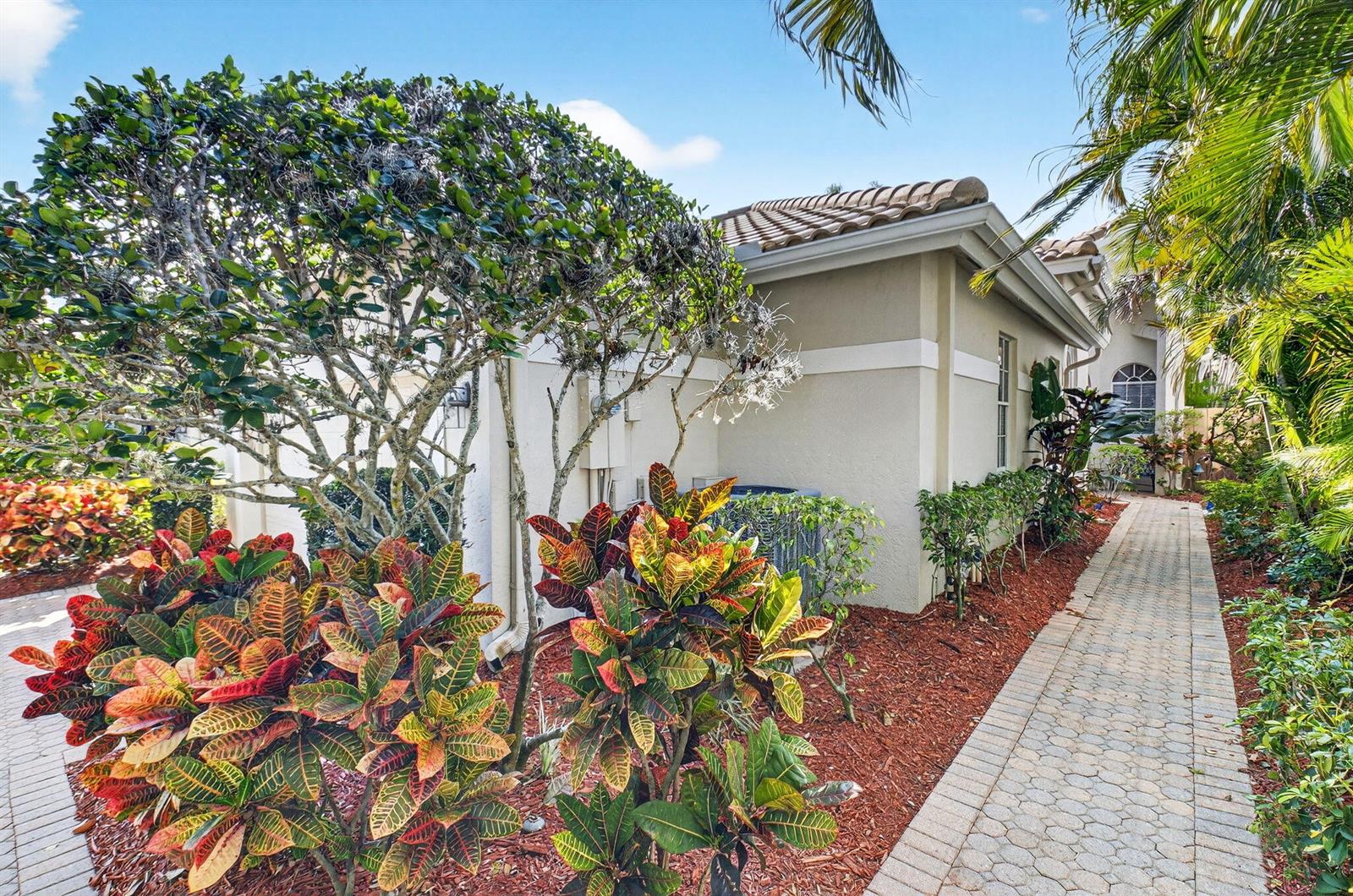 A paved walkway leads past colorful croton plants toward the side of a stucco house — 2476 NW 66th Drive, Boca Raton FL 33496, BOCA RATON, FL