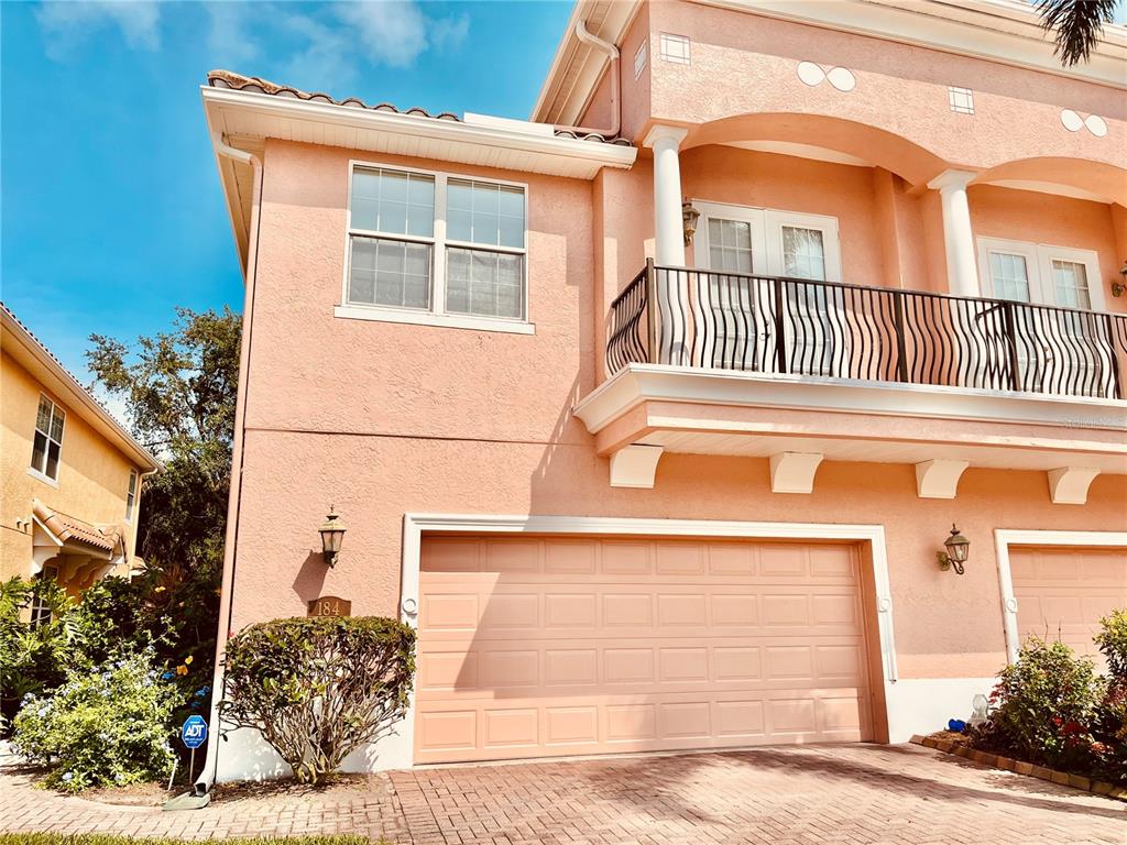 A two-story peach-colored house features a double garage, a second-floor balcony, and a brick driveway — 184 BANYAN BAY DRIVE, ST PETERSBURG, FL