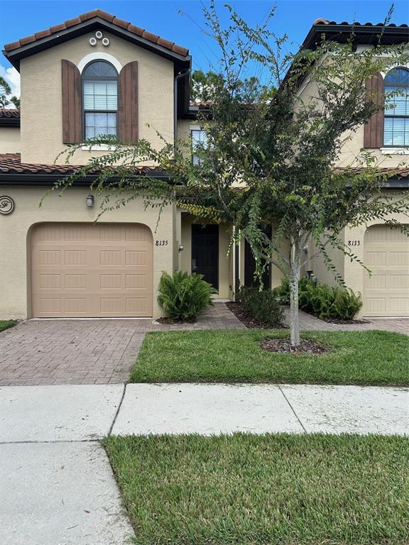 A two-story townhouse exterior features a tan stucco facade, a single-car garage, and a tree — 8135 ROSEVILLE BOULEVARD, DAVENPORT, FL