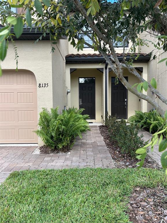 The exterior of a two-story townhouse features a tan garage, two dark doors, and landscaping — 8135 ROSEVILLE BOULEVARD, DAVENPORT, FL