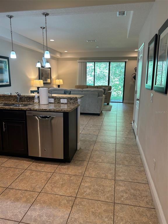 A kitchen with dark cabinets and granite countertops overlooks a living room with tile flooring — 8135 ROSEVILLE BOULEVARD, DAVENPORT, FL
