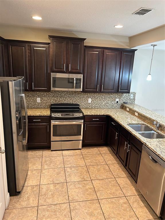 A kitchen features dark wood cabinets, granite countertops, stainless steel appliances, and tiled flooring — 8135 ROSEVILLE BOULEVARD, DAVENPORT, FL
