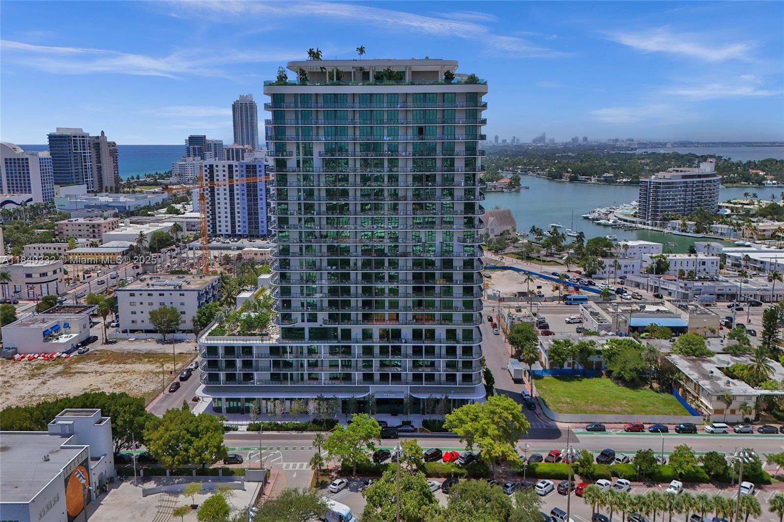An aerial view shows a modern high-rise residential building surrounded by urban infrastructure and water — 580 72nd St # 1208, Miami Beach FL 33141, MIAMI BEACH, FL