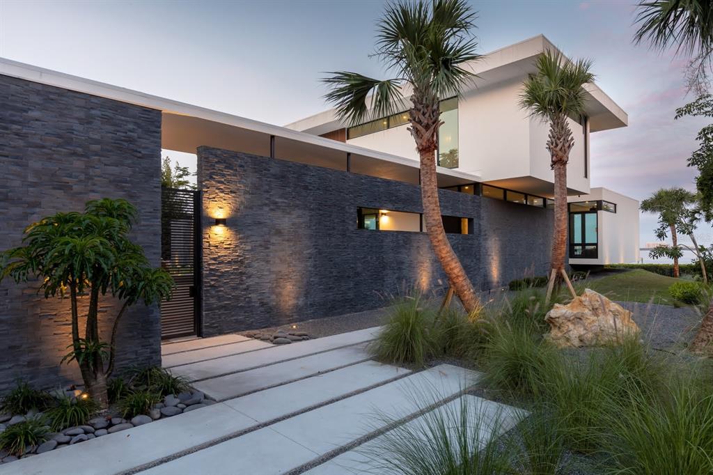 A modern house exterior features a dark stone wall, white upper level, and palm trees — 1500 BAYVIEW DRIVE, SARASOTA, FL
