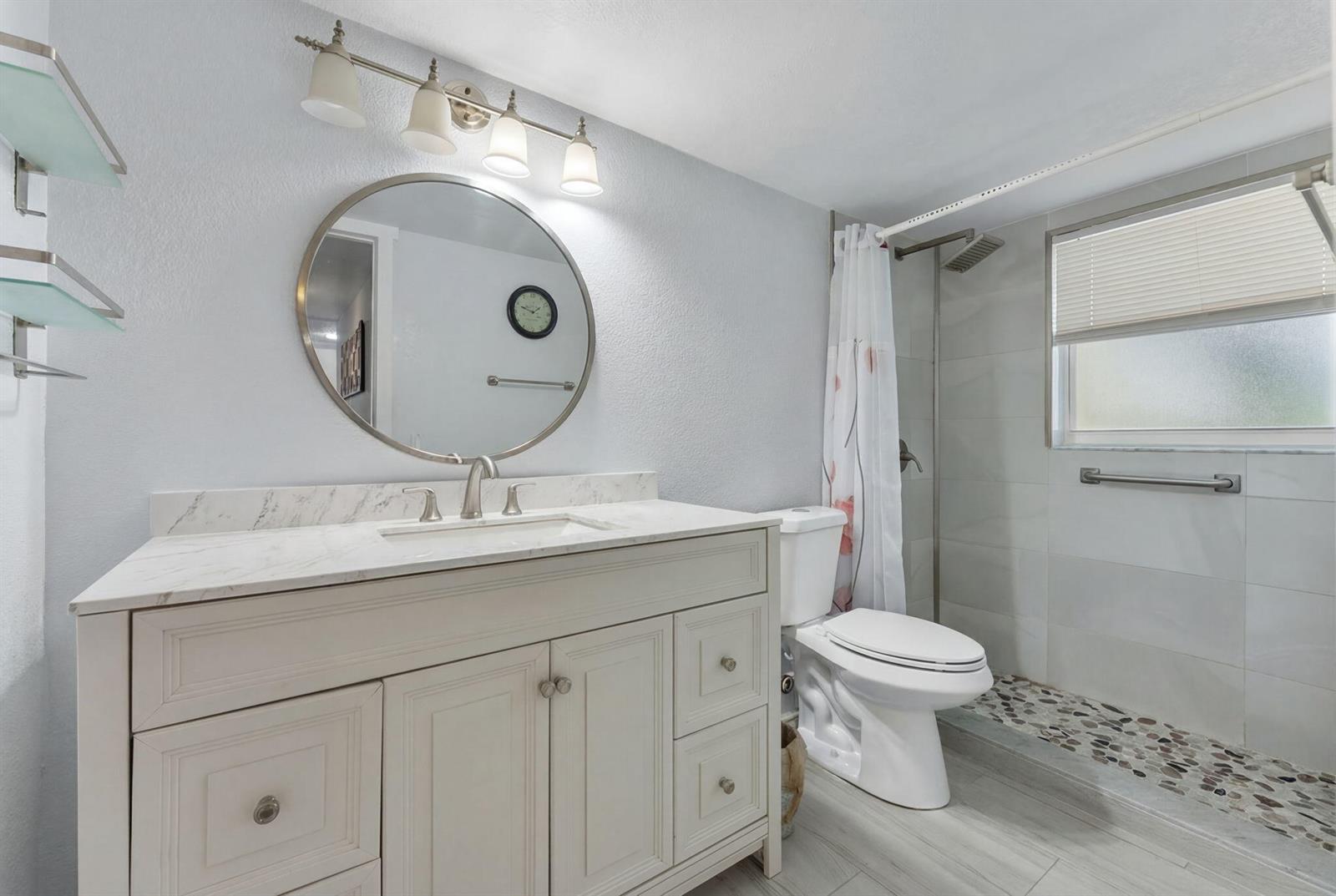 A bathroom features a white vanity with a marble top, round mirror, and walk-in shower — 1725 W 60th Street # F126, Hialeah FL 33012, HIALEAH, FL