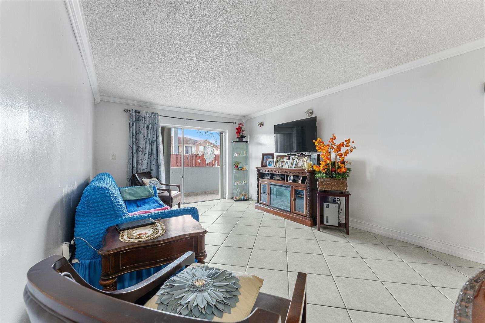 A living room with tile flooring, a blue sofa, a television console, and sliding doors — 1725 W 60th Street # F126, Hialeah FL 33012, HIALEAH, FL