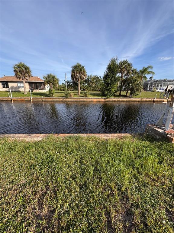 A metal boat davit stands on a concrete base beside a canal in a grassy yard — 3016 SHANNON DRIVE, PUNTA GORDA, FL