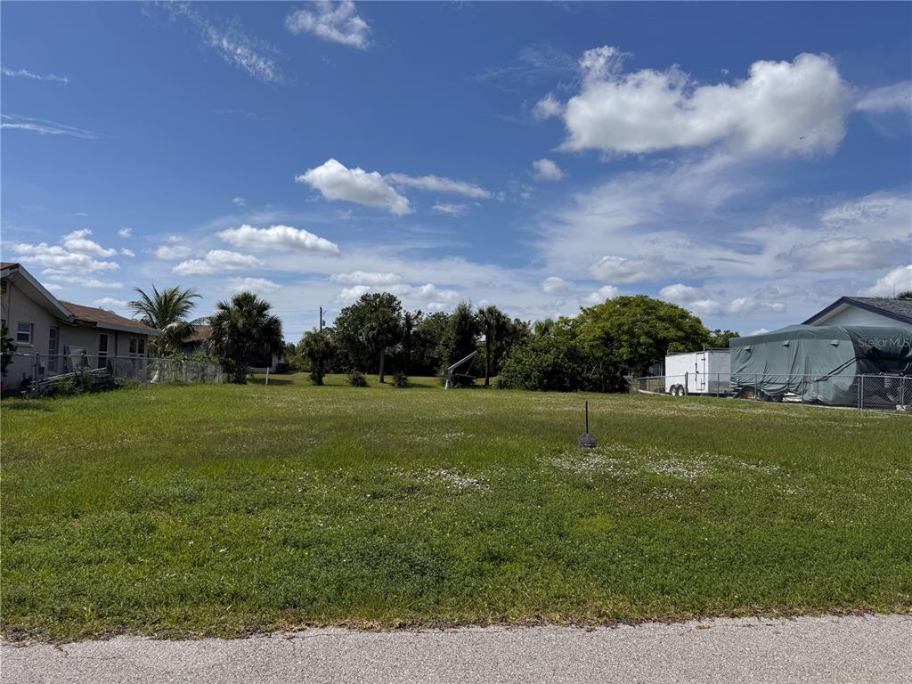 A canal separates a grassy yard from houses and palm trees under a blue sky — 3016 SHANNON DRIVE, PUNTA GORDA, FL