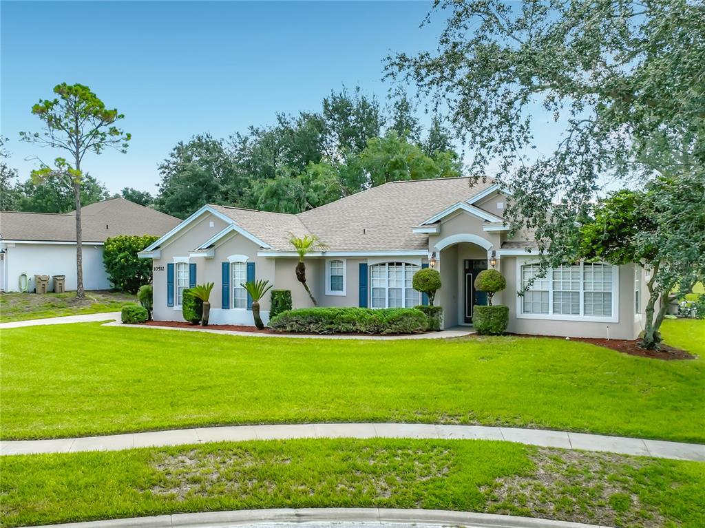 A single-story house with a beige exterior, blue shutters, and a manicured lawn — 10512 VIA MILANO COURT, CLERMONT, FL