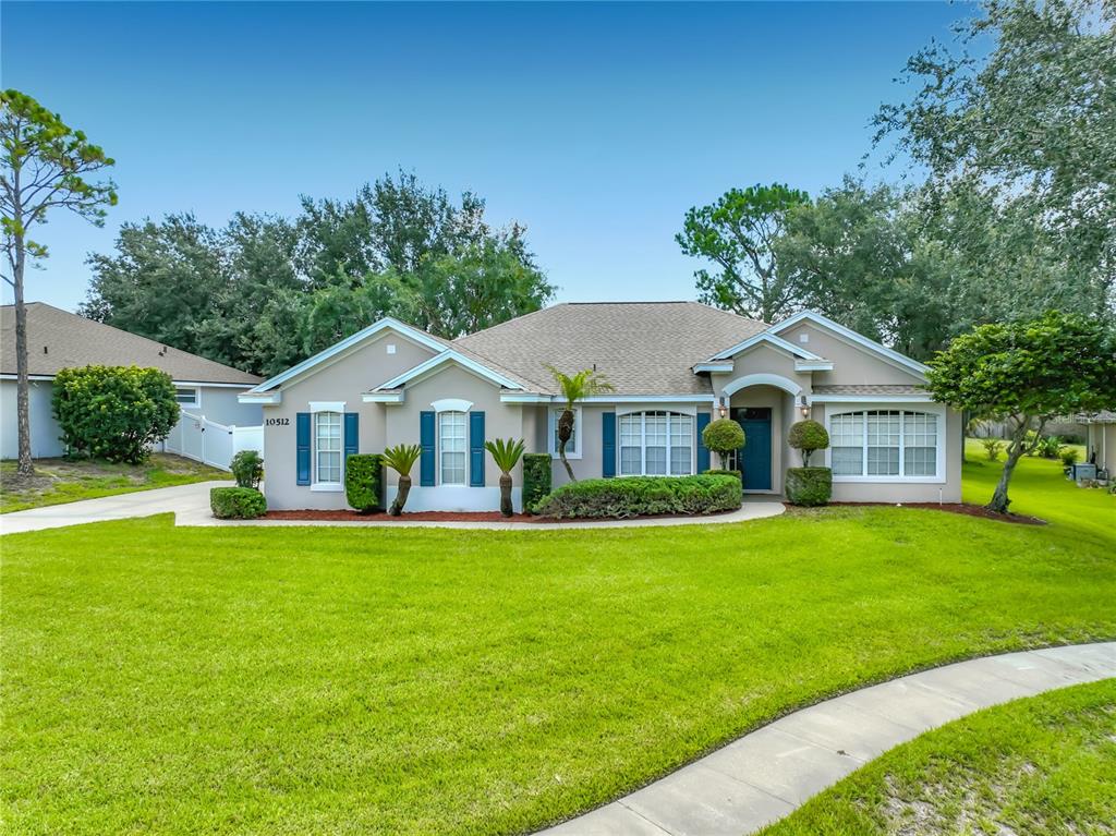 A single-story suburban house with a tan exterior, blue shutters, and a green lawn — 10512 VIA MILANO COURT, CLERMONT, FL