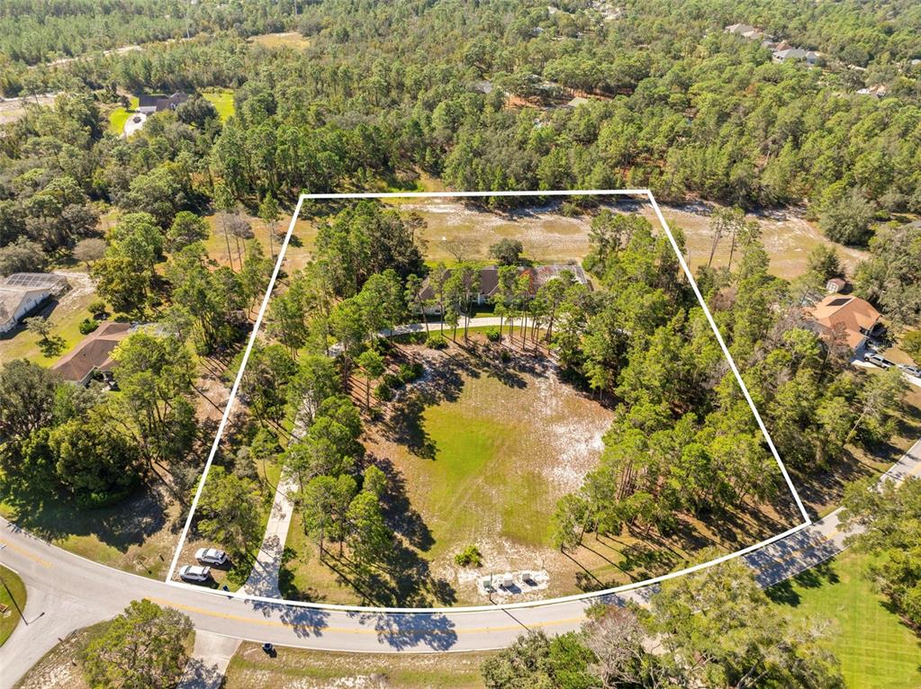 An aerial view shows a house situated on a large, wooded lot with a driveway — 11200 WOODLAND WATERS BOULEVARD, WEEKI WACHEE, FL