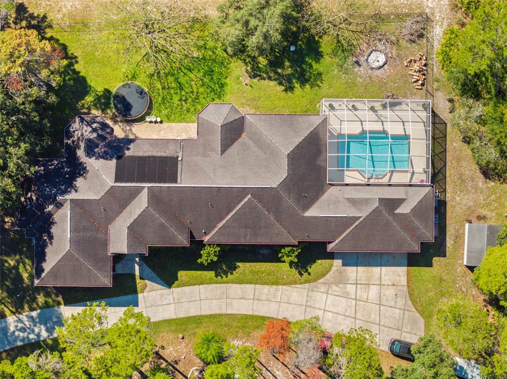 An aerial view shows a house with a shingled roof, pool enclosure, and driveway — 11200 WOODLAND WATERS BOULEVARD, WEEKI WACHEE, FL