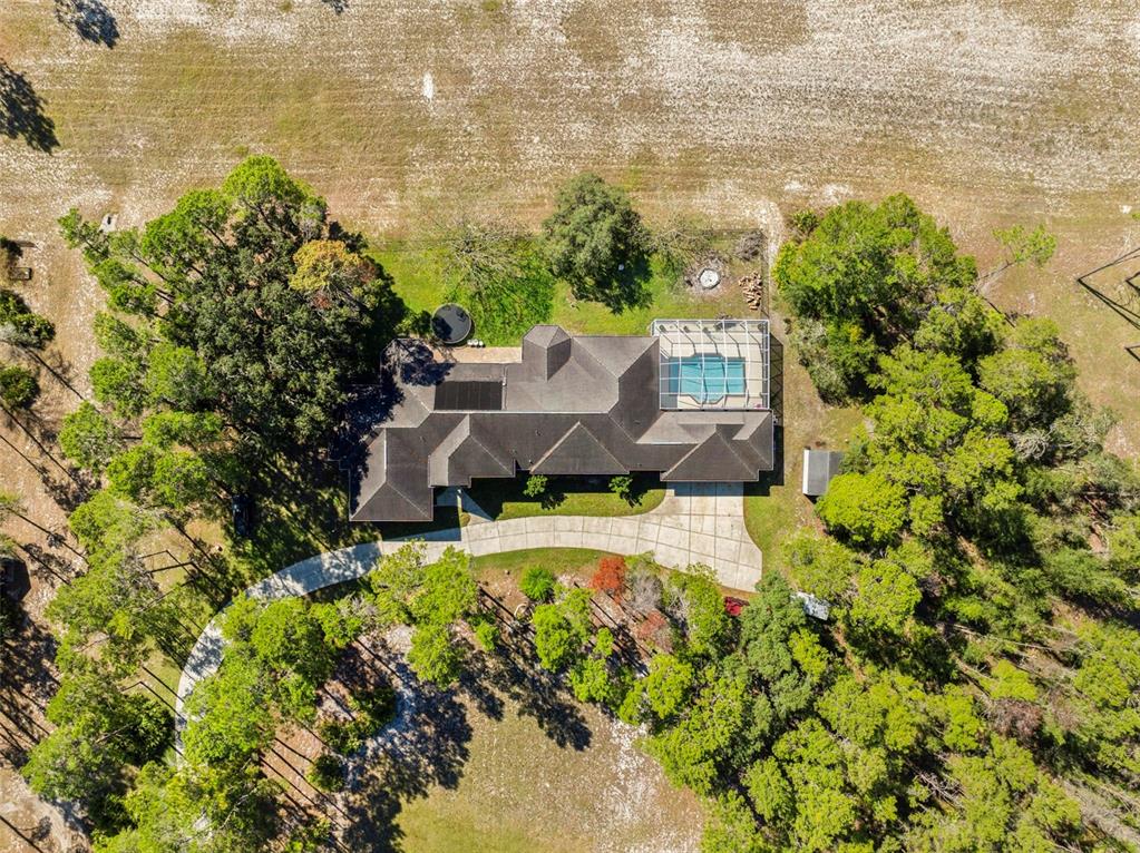 An aerial view shows a house with a screened pool surrounded by trees and grass — 11200 WOODLAND WATERS BOULEVARD, WEEKI WACHEE, FL