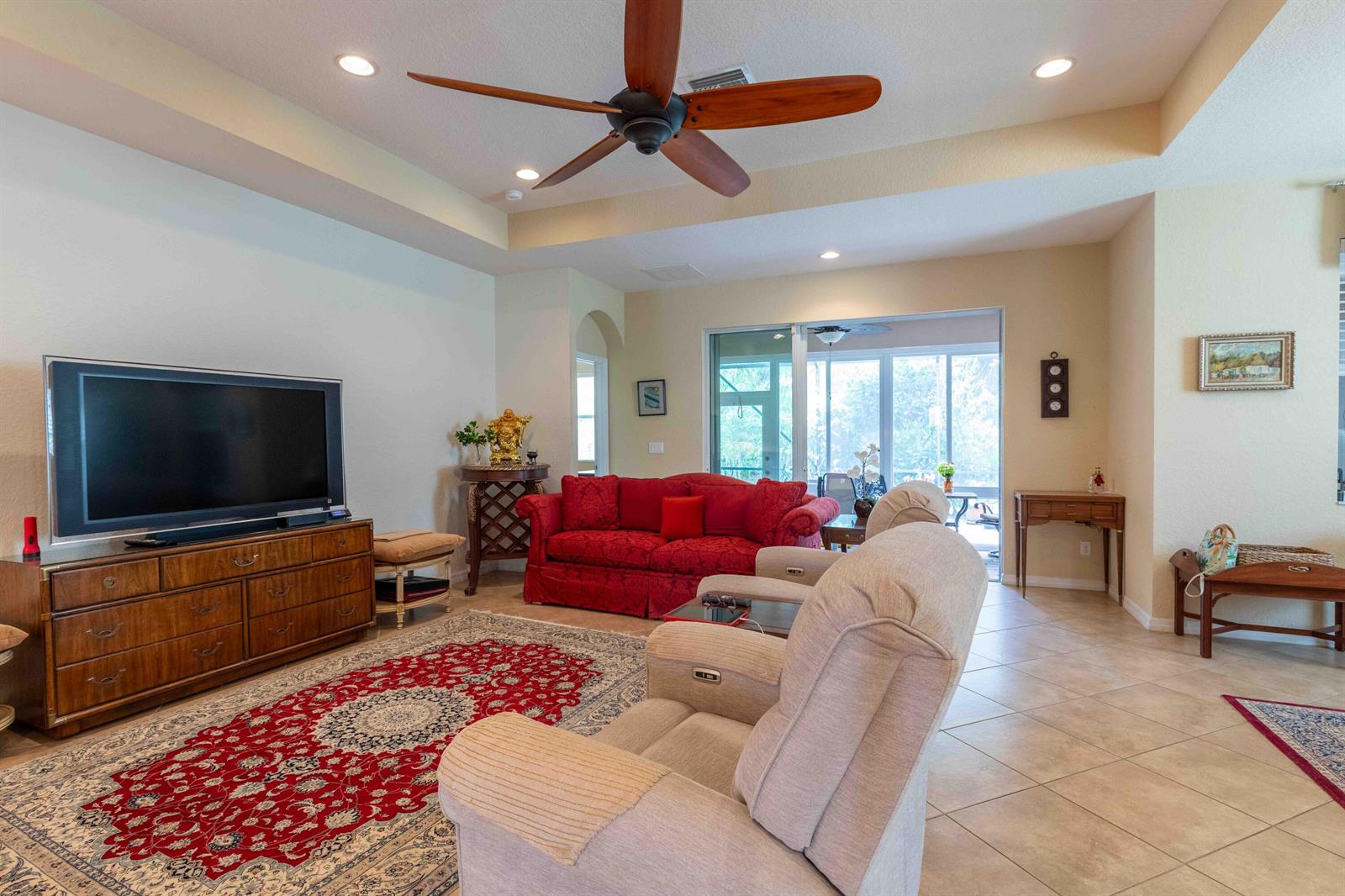 A living room features a red sofa, beige recliners, a large area rug, and a ceiling fan — 4376 NW Oakbrook Circle, Jensen Beach FL 34957, JENSEN BEACH, FL