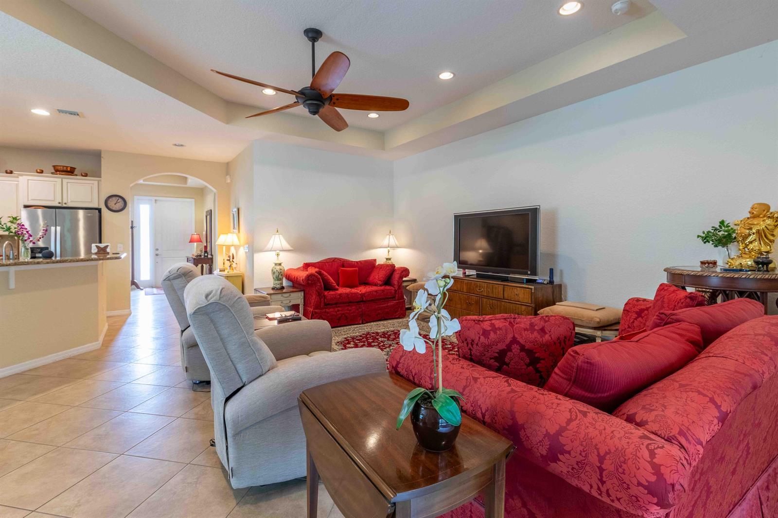 A living room features red patterned sofas, light-colored recliners, a ceiling fan, and tile flooring — 4376 NW Oakbrook Circle, Jensen Beach FL 34957, JENSEN BEACH, FL