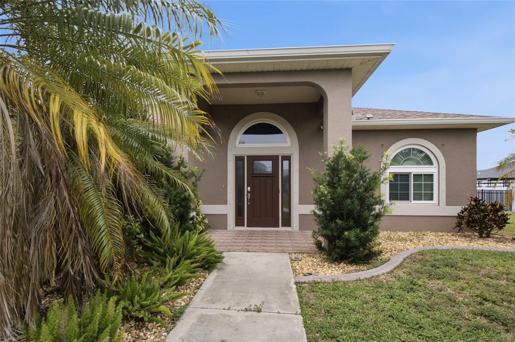 A tan house exterior features a brown front door, arched windows, and a palm tree — 219 NW 12TH LANE, CAPE CORAL, FL