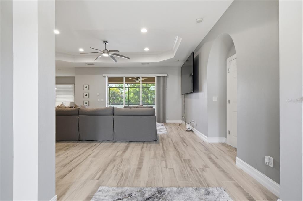 A living room with light wood-look flooring, a gray sectional sofa, and a tray ceiling — 219 NW 12TH LANE, CAPE CORAL, FL
